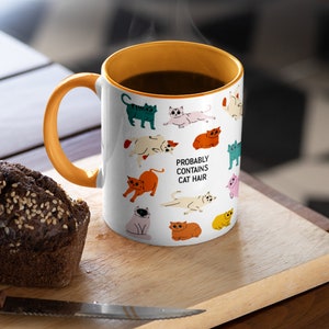 May include: White ceramic mug with an orange rim and handle. The mug features a pattern of colourful cats and the text "Probably Contains Cat Hair".