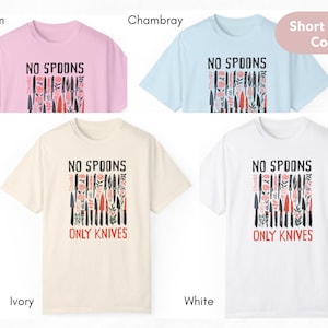 May include: Four short-sleeved t-shirts in different colours: blossom, ivory, white, and chambray. Each shirt features a graphic print of a row of knives with the text "No Spoons Only Knives".