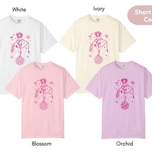 May include: Four short-sleeve t-shirts in white, ivory, blossom pink, and orchid purple. Each shirt features a pink graphic of a cowgirl on a disco ball with the text "Keep on Dancing".