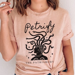 K&ouml;nnte beinhalten: Ein hellrosa T-Shirt mit einer schwarzen Grafik einer Frau mit Schlangen als Haaren. Der Text "Petrify The Patriarchy" ist unter der Grafik aufgedruckt.