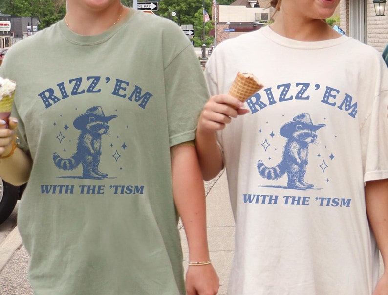 Peut inclure: Deux personnes portant des t-shirts avec un raton laveur portant un chapeau de cowboy et le texte "Rizz'em with the 'tism".