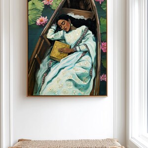 Puede incluir: Pintura al &oacute;leo de una persona dormida en un bote de madera, rodeada de nen&uacute;fares y flores de loto rosas. La persona lleva un vestido azul claro y sostiene un libro dorado. La obra est&aacute; enmarcada.