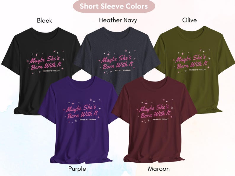 Puede incluir: Cinco camisetas de manga corta en diferentes colores con el texto "Maybe She's Born With It" impreso en la parte delantera. Los colores son negro, azul marino jaspeado, oliva, morado y granate.