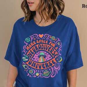 May include: A royal blue t-shirt featuring a colourful graphic design that reads "Make space for a neurodiverse universe". The graphic depicts a psychedelic eye with a spaceship, stars, and planets.