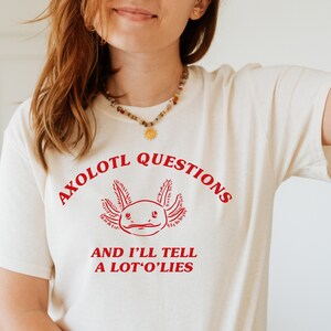 May include: A white t-shirt with a red axolotl graphic and the text "Axolotl Questions and I'll Tell A Lot O' Lies".