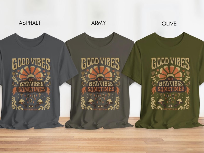 May include: Three t-shirts in different colors: asphalt, army, and olive. Each shirt features a graphic design with the text "Good Vibes But Bad Vibes Sometimes".