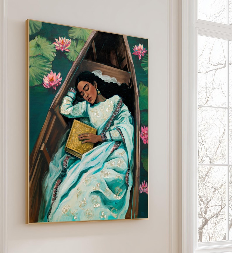 Puede incluir: Pintura al &oacute;leo de una persona con un sari azul claro, dormida en un bote de madera. La persona sostiene un libro dorado, rodeada de flores de loto rosas y hojas de nen&uacute;far verdes. La obra est&aacute; enmarcada en un marco dorado.