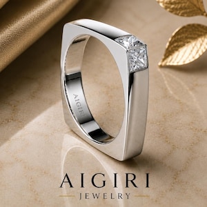 Op de afbeelding: Een zilveren ring met een vierkant ontwerp en twee vierkant geslepen diamanten. De ring is van de AIGIRI Jewelry collectie. De ring wordt gepresenteerd op een neutrale achtergrond met gouden accenten.