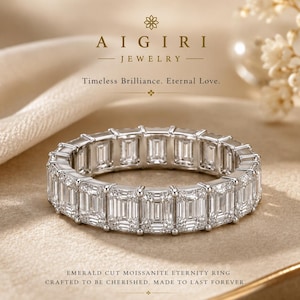 Op de afbeelding: Een eternity ring met een doorlopende band van smaragdgeslepen moissaniet stenen gezet in een zilverkleurig metaal. De tekst AIGIRI JEWELRY Timeless Brilliance. Eternal Love. en EMERALD CUT MOISSANITE ETERNITY RING CRAFTED TO BE CHERISHED. MADE TO LAST FOREVER. is zichtbaar.