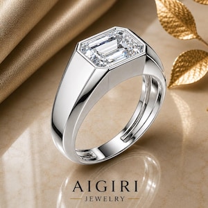 Op de afbeelding: Een zilveren ring met een grote, rechthoekige, heldere edelsteen. De ring heeft een modern ontwerp met een dikke band en een bezel setting. De merknaam "AIGIRI JEWELRY" staat onderaan de afbeelding.