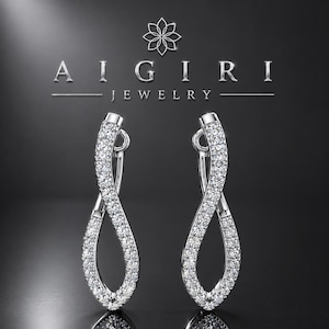 May include: A pair of silver-toned drop earrings featuring a twisted infinity loop design encrusted with small clear stones. The text AIGIRI JEWELRY is displayed above the earrings in a metallic font with a floral icon centred at the top.