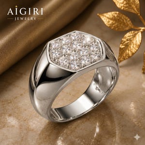 Puede incluir: Un anillo plateado con una cara hexagonal engastada con múltiples piedras preciosas pequeñas y claras. El anillo tiene una superficie pulida y reflectante. El nombre de la marca "AIGIRI JEWELRY" es visible.