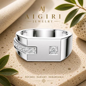 Könnte beinhalten: Ein silberner Ring mit einem quadratischen Diamanten und einer Reihe kleinerer Diamanten. Der Ring hat ein geometrisches Design, und der Text "AJ AIGIRI JEWELRY" ist sichtbar. Die Worte "REFINED. RADIANT. REMARKABLE." sind ebenfalls vorhanden.