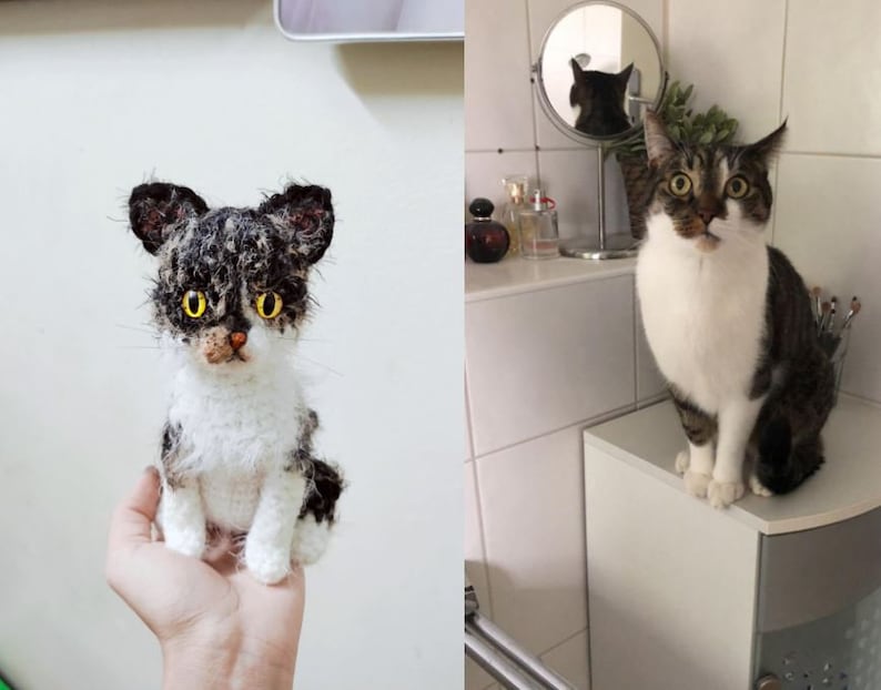 May include: A crocheted cat toy with black and white fur and yellow eyes. The toy is being held in a person's hand. A real cat with black and white fur and yellow eyes is sitting on a white counter.