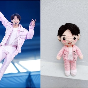 May include: A pink crocheted doll wearing a pink jacket and trousers. The doll has black hair and a smiling face.