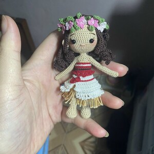 May include: A crocheted doll with brown hair, wearing a flower crown, a red and white striped top, and a white and brown skirt.