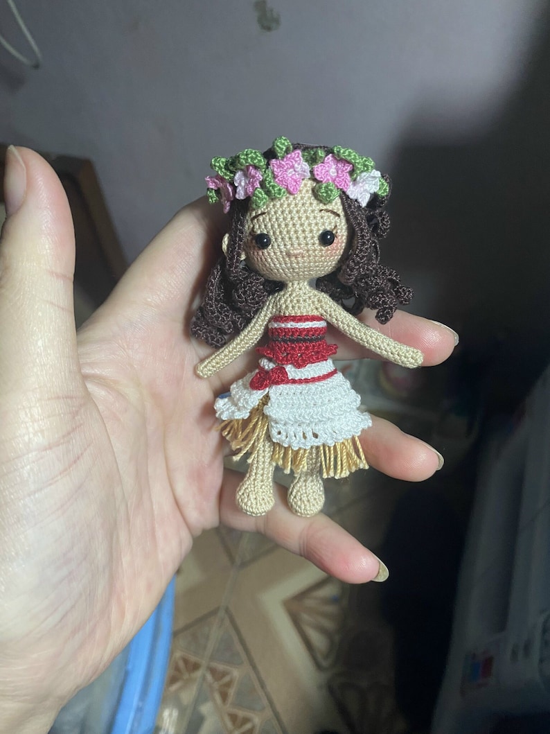 May include: A crocheted doll with brown hair, wearing a flower crown, a red and white striped top, and a white and brown skirt.