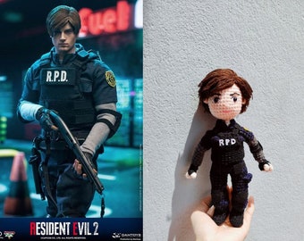 May include: A crocheted doll of a character from the Resident Evil video game series. The doll is wearing a black and blue police uniform with the letters "RPD" on the chest. The doll has brown hair and a light pink face.