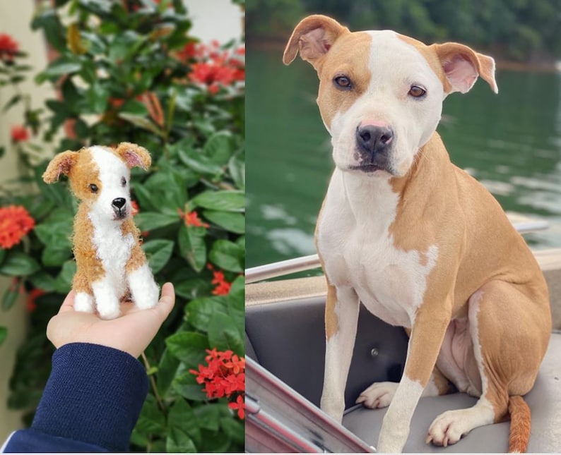 May include: A crocheted dog toy, brown and white, with a realistic appearance, is held in a person's hand. A real dog, brown and white, sits on a boat.