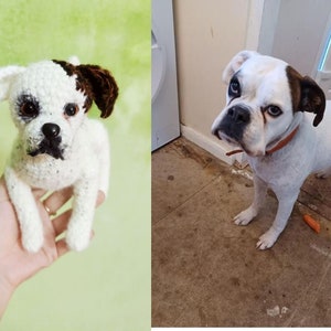 Op de afbeelding: Een gehaakt wit en bruin honden speelgoed met zwarte ogen en een zwarte neus. Het speelgoed wordt in de hand van een persoon gehouden.