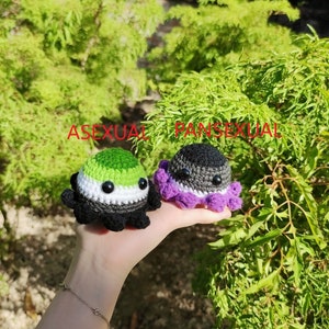 May include: Two crocheted octopus plushies, one with green, black, and white stripes representing the asexual pride flag and the other with black and purple stripes representing the pansexual pride flag.