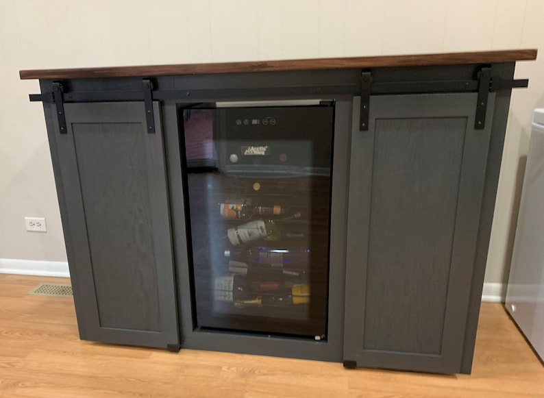 May include: A gray wooden cabinet with sliding barn doors and a built-in wine cooler. The cabinet has a dark wood countertop and black metal hardware.