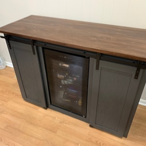 May include: A dark gray wooden cabinet with sliding barn doors and a built-in wine cooler. The cabinet has a dark brown wood countertop.