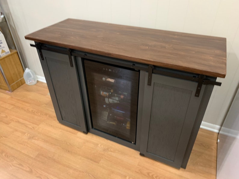 May include: A dark gray wooden cabinet with sliding barn doors and a built-in wine cooler. The cabinet has a dark brown wood countertop.