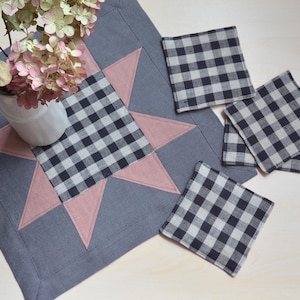 Może przedstawiać: Szary bieżnik z różowym wzorem gwiazdy i pasującymi czarno-białymi podkładkami w kratę. Biały wazon z suszonymi kwiatami stoi na bieżniku, tworząc rustykalną, wiejską estetykę.