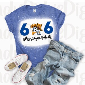 May include: A blue t-shirt with a white bleach design featuring the number 6, a mascot, and the text "Betsy Layne Bobcats".