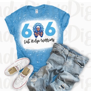 May include: A blue t-shirt with a white bleach design featuring the numbers 606 and the text "East Ridge Warriors". A Native American warrior mascot is depicted in the center of the design. The shirt is laid out on a white surface with a pair of white sneakers and blue jeans.