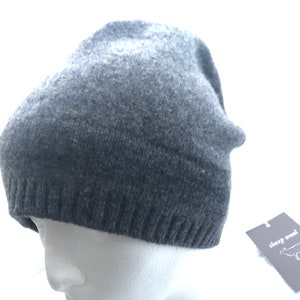 May include: A gray knitted beanie hat with a fold-over brim. The hat is made of sheep wool and has a small tag attached with the words "sheep wool" and a sheep illustration.