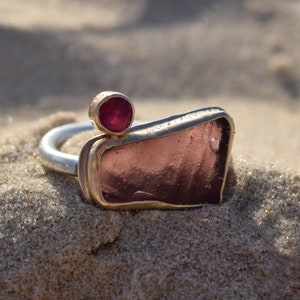 Puede incluir: Un anillo de plata con una piedra de vidrio rosa engastada en oro y una pequeña piedra roja en la parte superior.