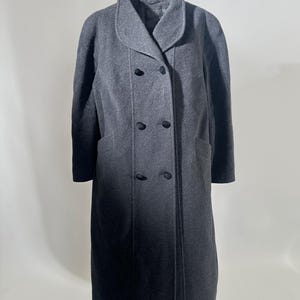 May include: A charcoal gray double-breasted coat with a wide collar and two rows of black buttons. The coat has two front pockets and a long, knee-length design. The fabric appears to be a wool blend.