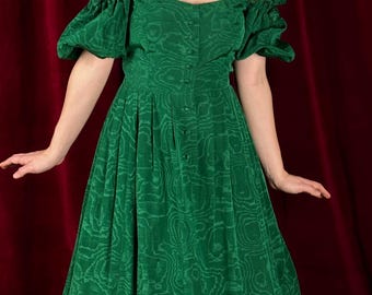 May include: A green off-the-shoulder dress with a button-up front and a swirling pattern. The dress has puffed sleeves and a flowing skirt.