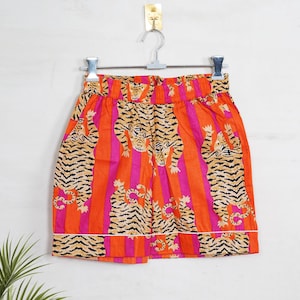 "Vibrant orange and pink vertical striped pajama set featuring a repeating tiger animal print. This 4-piece women's cotton nightwear collection includes a long-sleeve button-down shirt with collar and piping, full-length pajama pants, matching shorts, and a fabric envelope pouch. Indian block print style loungewear perfect for boho bridesmaid gifts, bachelorette parties, or summer sleepwear. Soft breathable fabric with funky safari design."