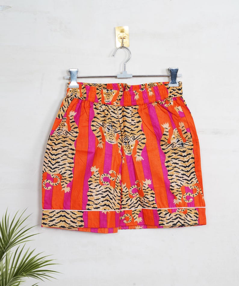 "Vibrant orange and pink vertical striped pajama set featuring a repeating tiger animal print. This 4-piece women's cotton nightwear collection includes a long-sleeve button-down shirt with collar and piping, full-length pajama pants, matching shorts, and a fabric envelope pouch. Indian block print style loungewear perfect for boho bridesmaid gifts, bachelorette parties, or summer sleepwear. Soft breathable fabric with funky safari design."