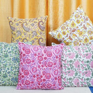 Puede incluir: Cinco cojines decorativos con patrones florales. Los cojines están dispuestos en una fila sobre una superficie azul claro. Los cojines están hechos de algodón y tienen una variedad de colores, incluyendo rosa, azul, verde, amarillo y blanco.