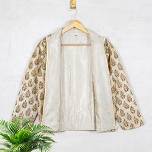 May include: A cream-colored jacket with a floral print on the sleeves. The jacket is unzipped and has a smooth, satin-like lining.