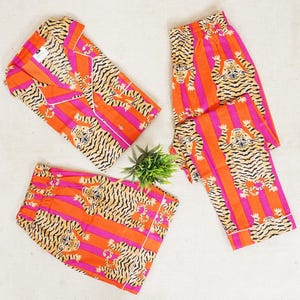 "Vibrant orange and pink vertical striped pajama set featuring a repeating tiger animal print. This 4-piece women's cotton nightwear collection includes a long-sleeve button-down shirt with collar and piping, full-length pajama pants, matching shorts, and a fabric envelope pouch. Indian block print style loungewear perfect for boho bridesmaid gifts, bachelorette parties, or summer sleepwear. Soft breathable fabric with funky safari design."