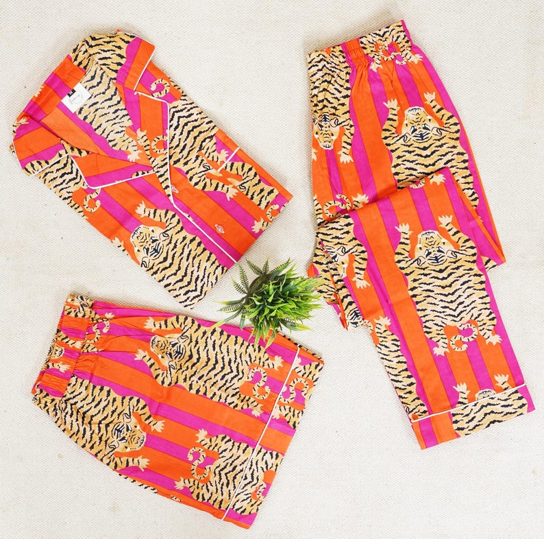 "Vibrant orange and pink vertical striped pajama set featuring a repeating tiger animal print. This 4-piece women's cotton nightwear collection includes a long-sleeve button-down shirt with collar and piping, full-length pajama pants, matching shorts, and a fabric envelope pouch. Indian block print style loungewear perfect for boho bridesmaid gifts, bachelorette parties, or summer sleepwear. Soft breathable fabric with funky safari design."