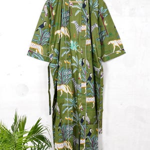 May include: Olive green robe with a jungle-themed print featuring leopards, zebras, toucans, and palm trees. The robe has white trim and a matching belt. The robe is hanging on a wooden hanger.