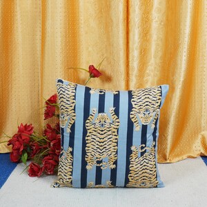 May include: A blue and white striped throw pillow with a repeating pattern of orange tigers. The tigers are facing forward with their paws up in the air.