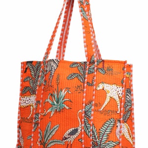 May include: Orange tote bag with a quilted texture and a white and orange striped trim. The bag features a colorful print of animals and plants, including zebras, leopards, flamingos, and palm trees.