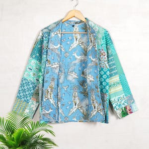 May include: A blue and green patchwork quilted jacket with a floral print lining. The jacket has long sleeves and a relaxed fit.