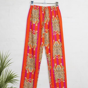 "Vibrant orange and pink vertical striped pajama set featuring a repeating tiger animal print. This 4-piece women's cotton nightwear collection includes a long-sleeve button-down shirt with collar and piping, full-length pajama pants, matching shorts, and a fabric envelope pouch. Indian block print style loungewear perfect for boho bridesmaid gifts, bachelorette parties, or summer sleepwear. Soft breathable fabric with funky safari design."