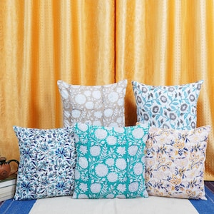 Puede incluir: Cinco cojines decorativos con patrones florales. Los cojines están dispuestos en una fila sobre una superficie blanca. Los cojines son de varios colores, incluyendo blanco, beige, azul, verde y amarillo.