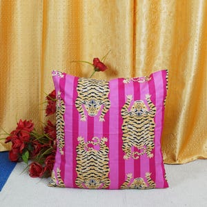 May include: Pink and yellow striped throw pillow with a tiger print. The tiger is facing upwards with its paws in the air.