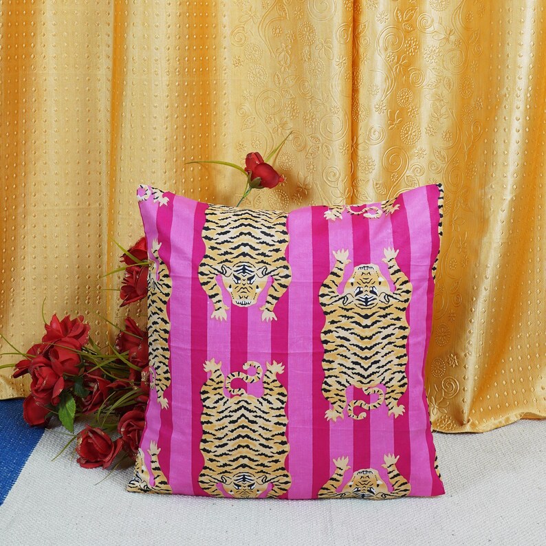 May include: Pink and yellow striped throw pillow with a tiger print. The tiger is facing upwards with its paws in the air.
