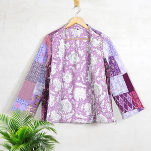 May include: A purple and white patchwork quilted jacket with a floral print lining. The jacket has a mandarin collar and long sleeves.